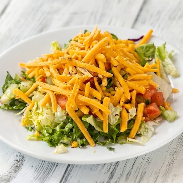 A fresh garden salad with shredded cheddar cheese, diced tomatoes, and black pepper on a white plate.