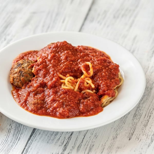 Spaghetti with a rich red marinara sauce and a large meatball on a white plate.