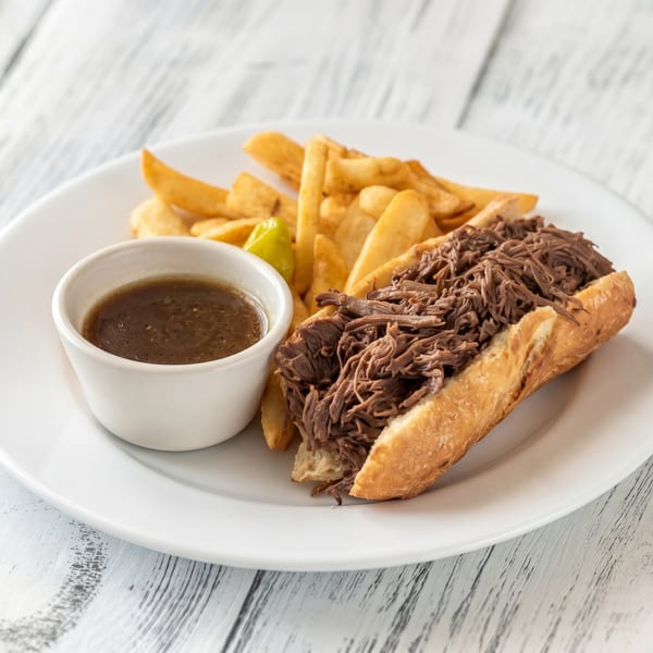 Shredded beef sandwich with a side of fries and a small bowl of gravy on a white plate.