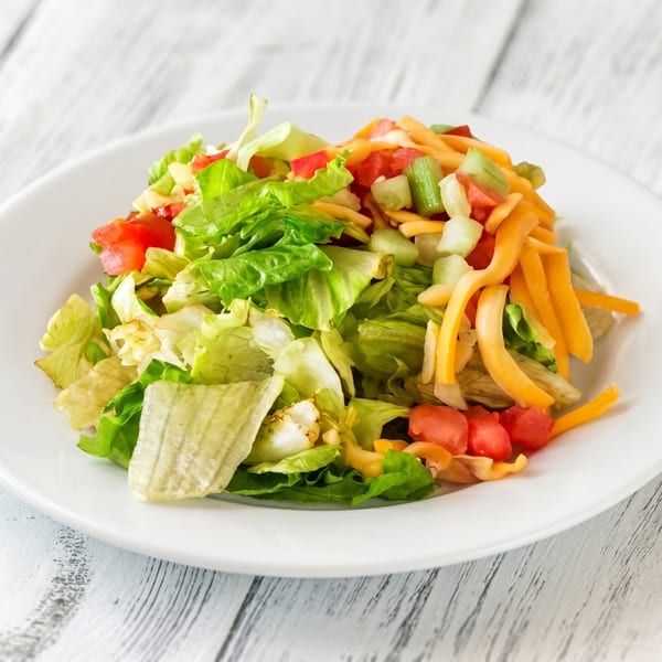 Fresh garden salad with lettuce, diced tomatoes, cucumbers, and shredded cheddar cheese on a white plate.